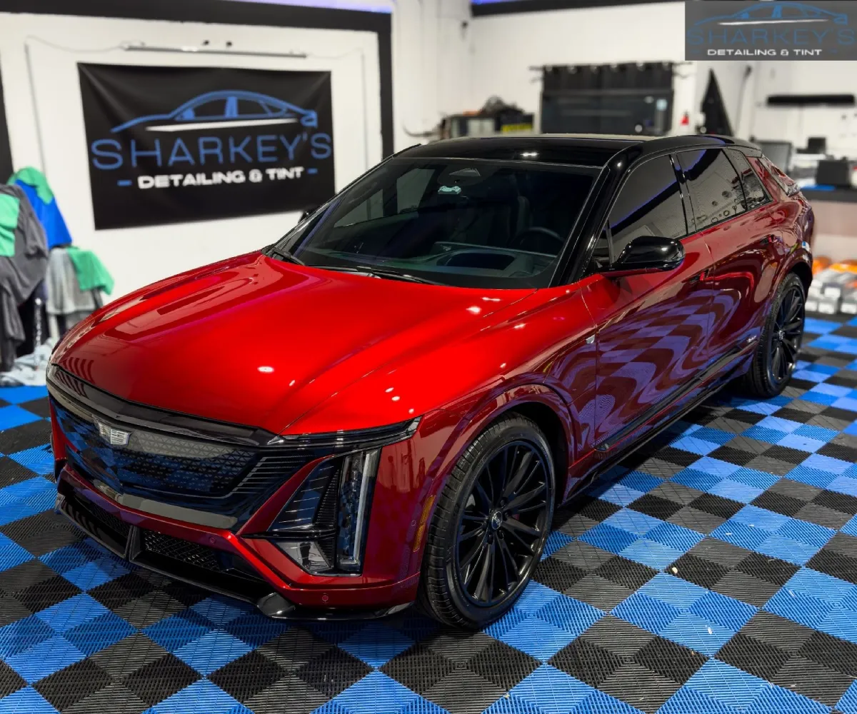 High-gloss red Cadillac Lyriq electric SUV with a black roof and black wheels parked on a blue-and-black tiled floor inside an auto detailing garage.